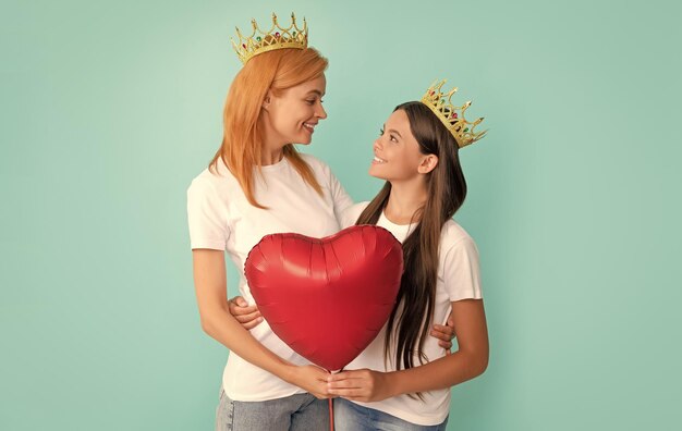 Gelukkige vrouw en meisje in kronen glimlachen naar elkaar met hartballon Valentijnsdag