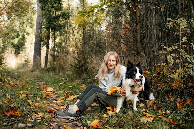 Gelukkige vrouw en zwart-witte border collie-hond in de herfstbos