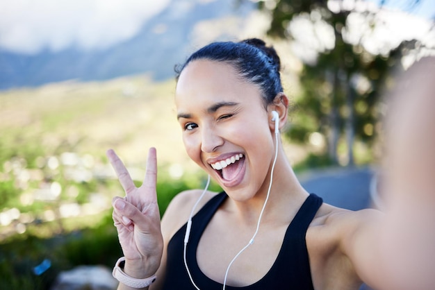 Gelukkige vrouw fitness en selfie met vredesteken voor profielfoto op sociale media of online post in de natuur Portret van grappige vrouwelijke persoon of hardloper met leuke uitdrukking voor foto of vlog buitenshuis