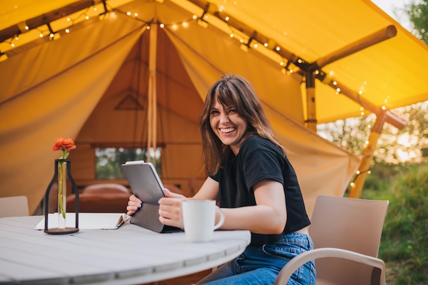 Gelukkige vrouw freelancer met behulp van een laptop op een gezellige glamping tent op een zonnige dag luxe camping tent voor buiten zomervakantie en vakantie lifestyle concept