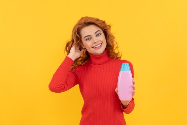 Gelukkige vrouw gebruikt douchegel. positief meisje krullend haar houdt shampoofles vast. haar conditioner