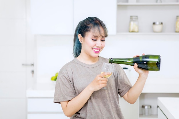 Gelukkige vrouw giet champagne in een glas in de keuken