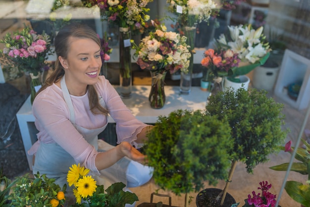 gelukkige vrouw het verzorgen van bloemen in bloemenwinkel