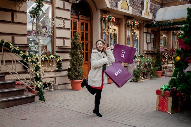 Gelukkige vrouw houdt papieren zakken met symbool van verkoop in de winkels met verkoop met Kerstmis
