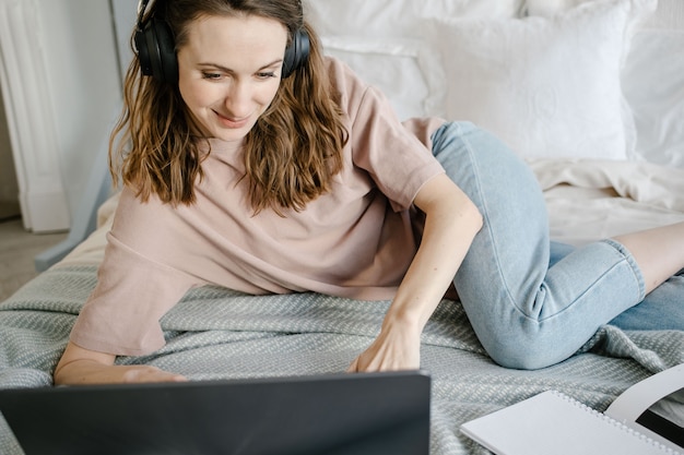 Gelukkige vrouw in casual met de koptelefoon die op afstand vanuit huis op een laptop werkt