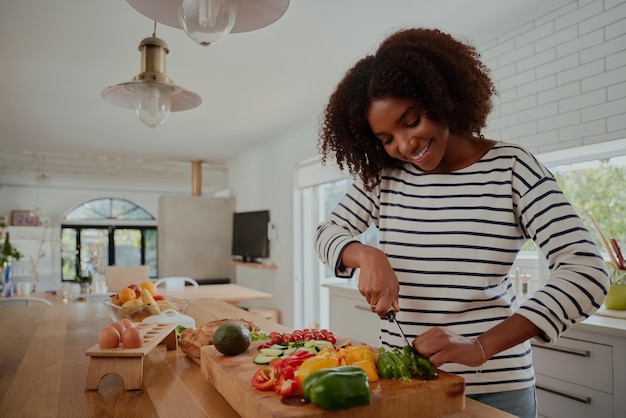 Gelukkige vrouw in de keuken met een mes om verse groene capsicum in plakjes te snijden