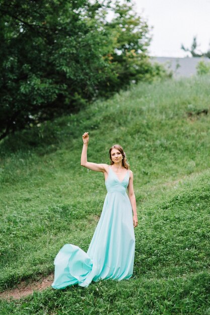 Gelukkige vrouw in een turquoise lange jurk in een groen park