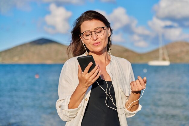 Gelukkige vrouw in koptelefoon luisteren naar muziek met behulp van smartphone op strand