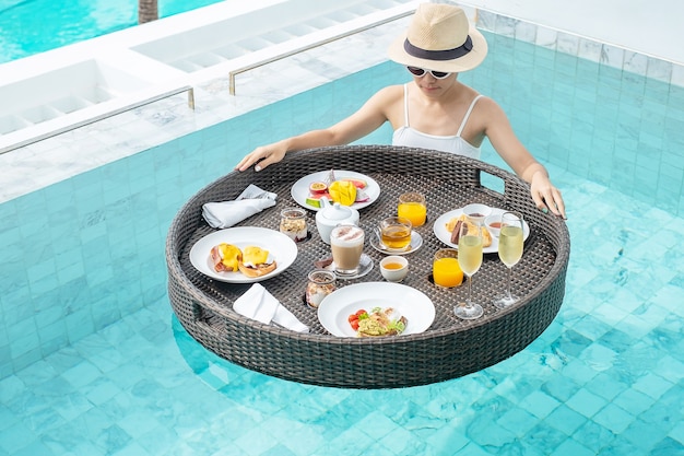 Gelukkige vrouw in witte zwembroek met drijvend ontbijt dienblad in luxehotel zwembad