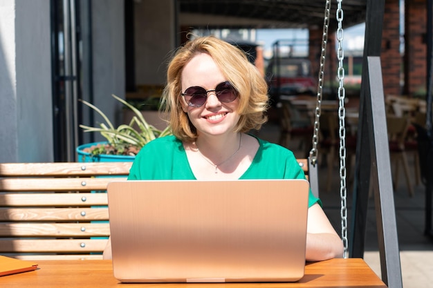 Gelukkige vrouw in zonnebril met toepassing op digitale laptop in een straatcafé