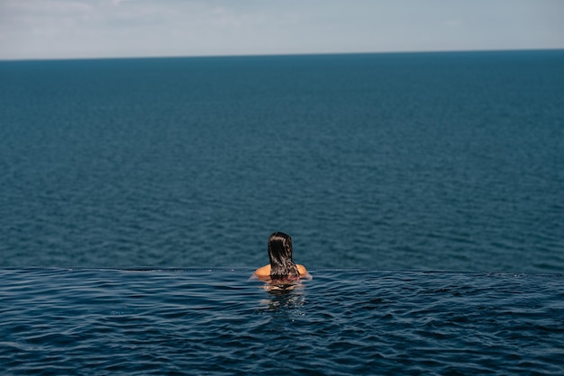 Gelukkige vrouw in zwembroek zwemmen in infinity pool tegen strandboulevard