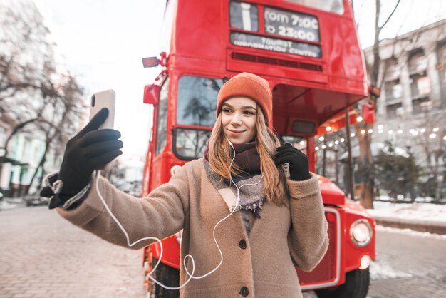Gelukkige vrouw is een toerist in warme kleren, gefotografeerd op de achtergrond van een rode bus