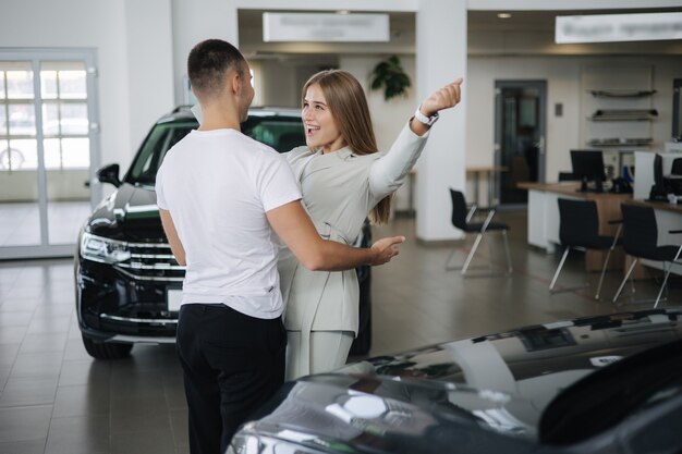 Gelukkige vrouw knuffelt zijn man nadat hij een auto in de autoshowroom heeft gekocht, man en vrouw kopen nieuwe auto