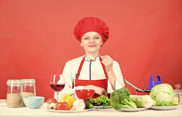 Gelukkige vrouw koken gezond voedsel door recept biologisch eten en vegetarische huisvrouw professionele chef-kok op rode achtergrond restaurant menu Dieet vrouw in kok hoed Vegetarisch dieet concept