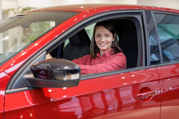 Gelukkige vrouw koopt een rode auto bij een autodealer, ondertekent een inruilcontract en overhandigt sleutels handen schudden