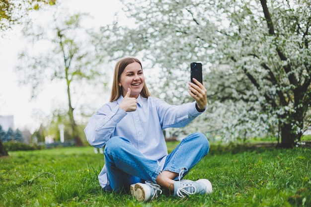 Gelukkige vrouw lopen met behulp van slimme telefoon in een stadsstraat Zakenvrouw met zonnebril gebruikt mobiele telefoon buitenshuis onder bloeiende boom meisje bericht aan het typen chatten scrollen webpagina kijken camera