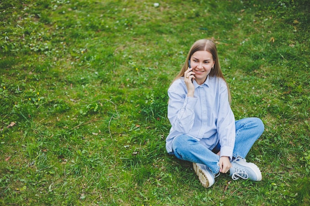 Gelukkige vrouw lopen met behulp van slimme telefoon in een stadsstraat Zakenvrouw met zonnebril gebruikt mobiele telefoon buitenshuis onder bloeiende boom meisje bericht aan het typen chatten scrollen webpagina kijken camera