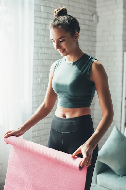 Gelukkige vrouw maakt haar fitnesstraining af en haalt haar mat van de vloer