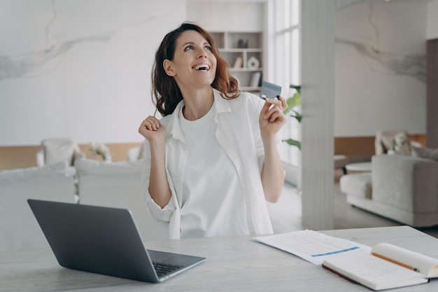 Gelukkige vrouw met bankcreditcard kreeg cashback-bonus met behulp van online bankservice op laptop