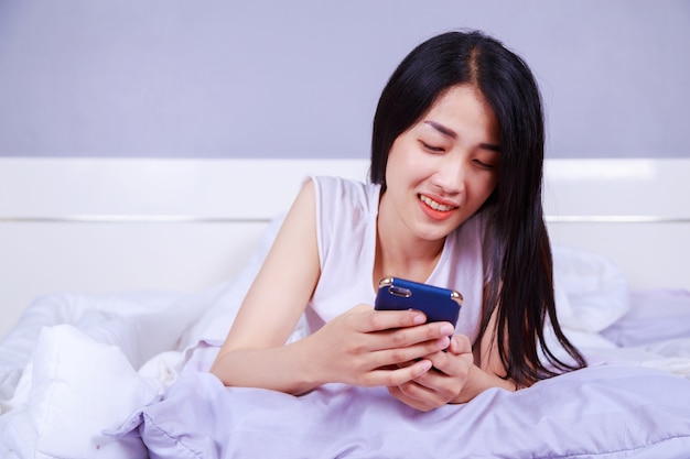 gelukkige vrouw met behulp van een telefoon in haar hand op bed in de slaapkamer