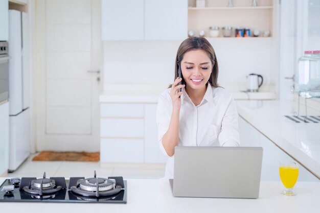 Gelukkige vrouw met behulp van mobiele telefoon en laptop in de keuken