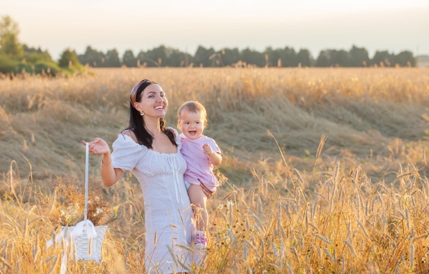 Gelukkige vrouw met dochtertje op zomerveld bij zonsondergang