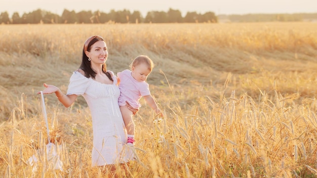 Gelukkige vrouw met dochtertje op zomerveld bij zonsondergang