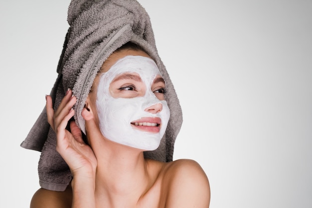 Gelukkige vrouw met een handdoek op haar hoofd bracht een masker op haar gezicht aan