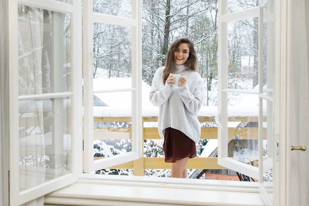 Gelukkige vrouw met een kopje warme drank op het balkon op winterdag