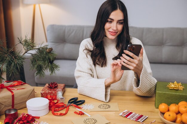 Gelukkige vrouw met een smartphone in de buurt van cadeautjes en wazig decor thuis