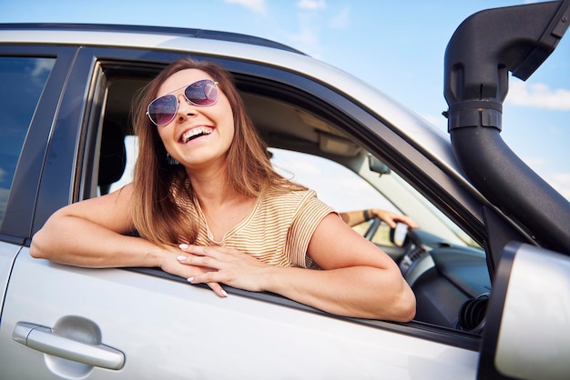 Gelukkige vrouw met een zonnebril die door het raam van de auto kijkt.