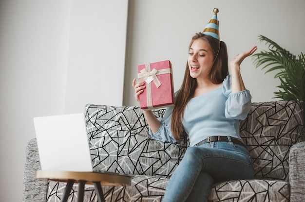 Gelukkige vrouw met geschenkdoos aanwezig en verrast tijdens online kerstviering via laptop