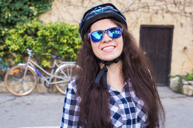 Gelukkige vrouw met helm en zonnebril die tegen fiets en straat stellen