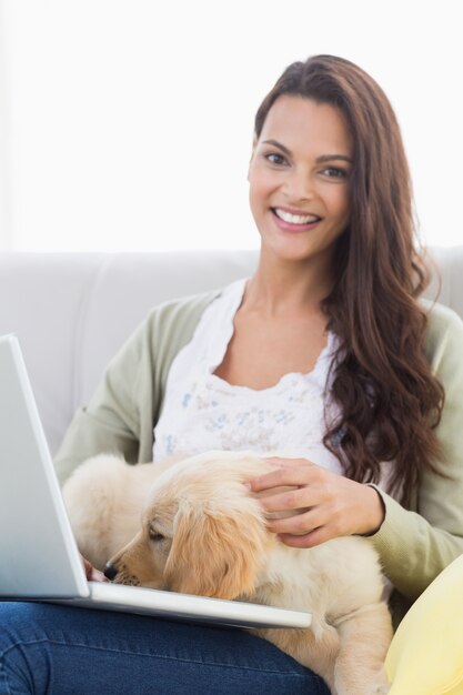 Gelukkige vrouw met hond die laptop op bank met behulp van