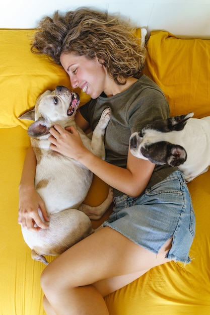 gelukkige vrouw met honden in bed. Bovenaanzicht van een jonge vrouw die een paar Franse buldoggen thuis knuffelt.