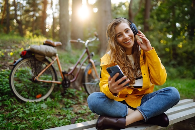 Gelukkige vrouw met koptelefoon, smartphone, fietst in een zonnig park, actieve levensstijl, rust.