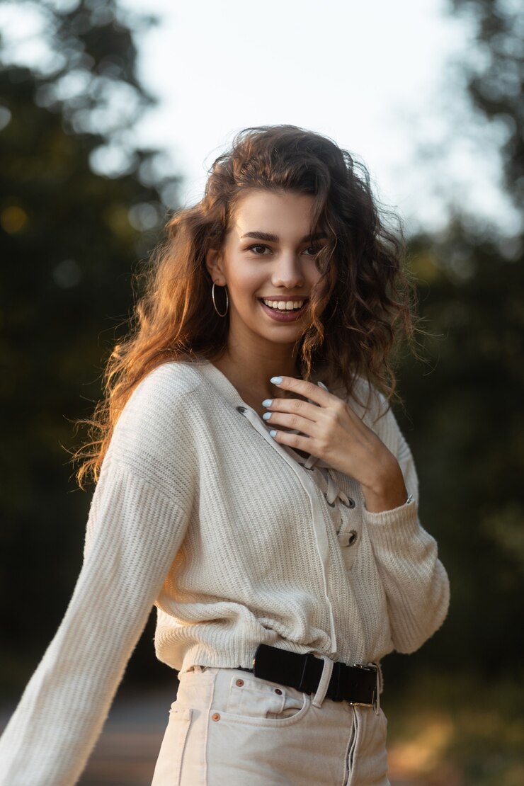 Foto gelukkige vrouw met krullend haar en mooie glimlach met tanden in modieuze gebreide trui buitenshuis. mooi lachend gezicht