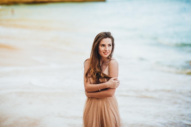 gelukkige vrouw met rug in een gele jurk staande op het strand en de zee bij zonsondergang