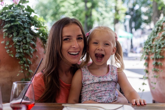 Gelukkige vrouw met schreeuwend blond meisje achter een cafetariatafel.