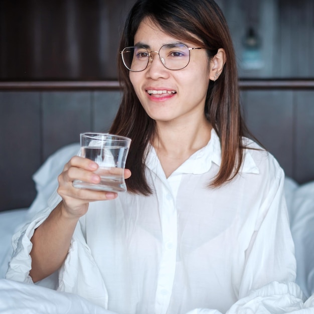 Gelukkige vrouw met waterglas vrouw die zuiver water drinkt op bed thuis Gezonde verfrissing levensstijl concept