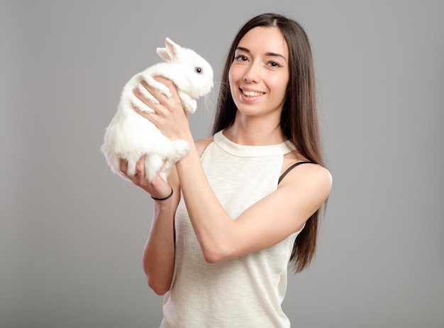 Gelukkige vrouw met wit konijn geïsoleerd op een grijze achtergrond