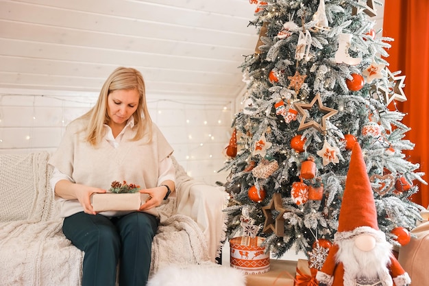 Gelukkige vrouw moeder bereidt zich voor op kerstmis, nieuwjaar pakt geschenken thuis terwijl ze in de buurt van de kerstboom zit. wintervakantie, woondecoratieconcept