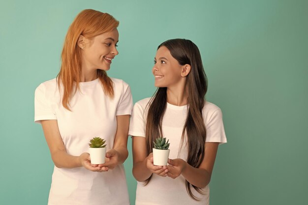 Gelukkige vrouw moeder en dochter kind glimlach met kamerplanten blauwe achtergrond verzorgen