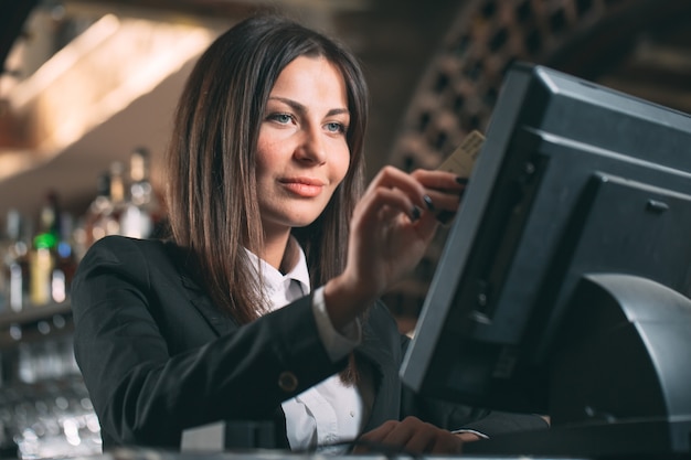 gelukkige vrouw of ober of manager in schort aan balie met kassa werken bij bar of coffeeshop