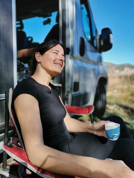 Gelukkige vrouw ontspannen op een openluchtcamping met een kopje koffie.