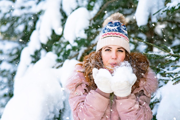 Gelukkige vrouw op de achtergrond van de bossneeuw valt op het meisje dat het vrouwtje in de winter glimlacht