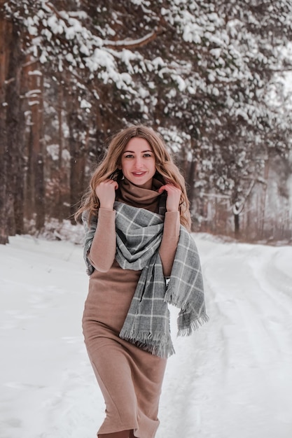 Gelukkige vrouw op de winter forest achtergrond. Jong mooi meisje in het bos buiten. Portret van een vrolijke mooie vrouw. Wintermode. Jurk met sjaal