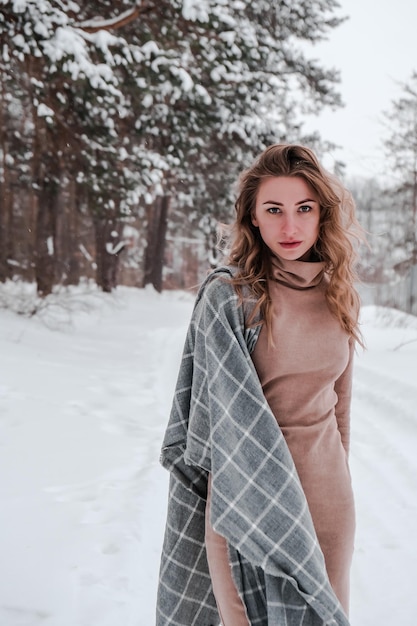 Gelukkige vrouw op de winter forest achtergrond. Jong mooi meisje in het bos buiten. Portret van een vrolijke mooie vrouw. Wintermode. Jurk met sjaal