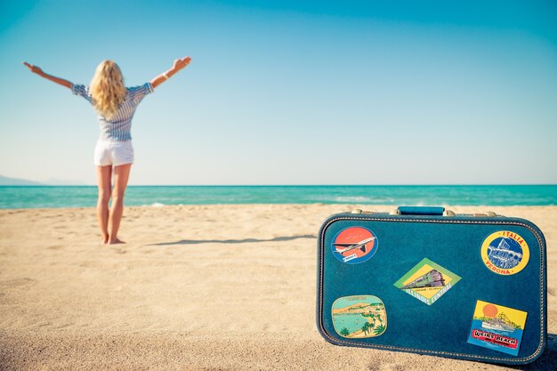 Gelukkige vrouw op het strand met een koffer met stickers erop