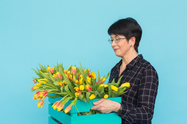 Gelukkige vrouw op middelbare leeftijd die met glazen doos tulpen in blauw houden